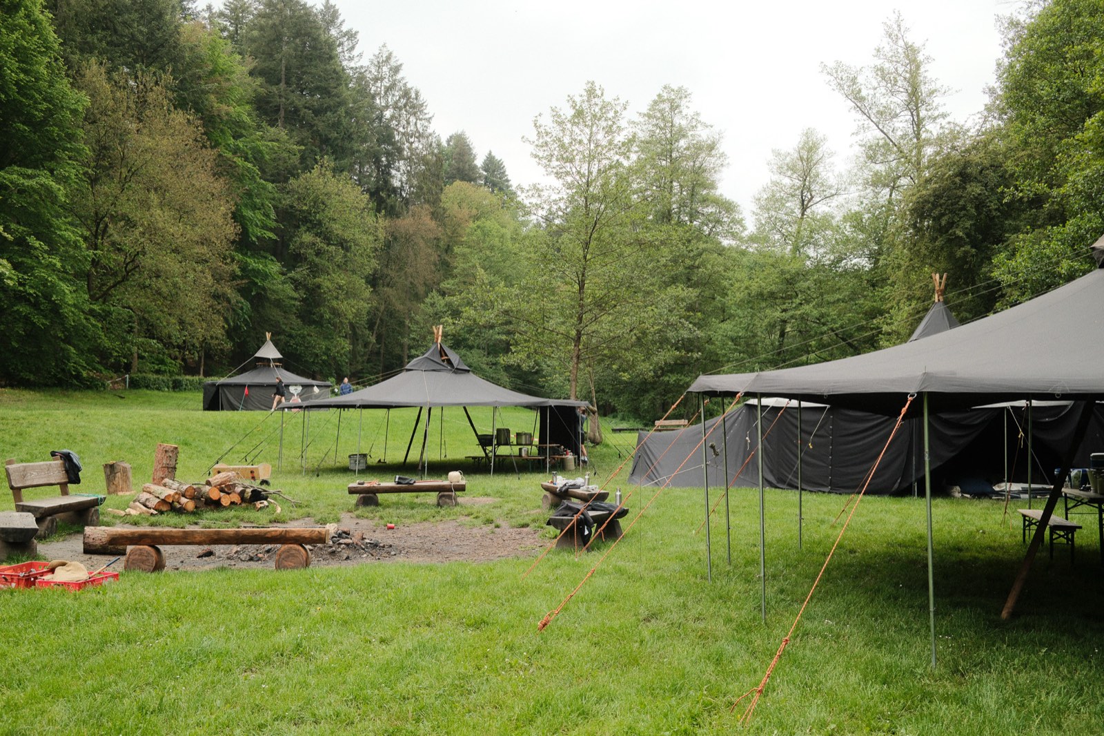 Lagerplatz mit schwarzen Jurten und einer Feuerstelle auf einer Waldwiese